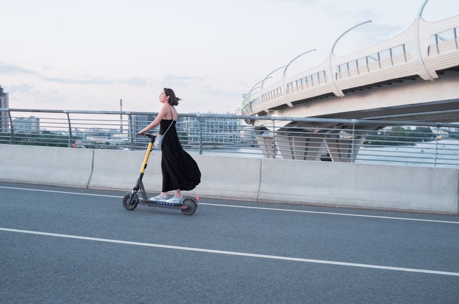 A woman enjoys a ride on an electric scooter across a modern urban bridge at sunset.