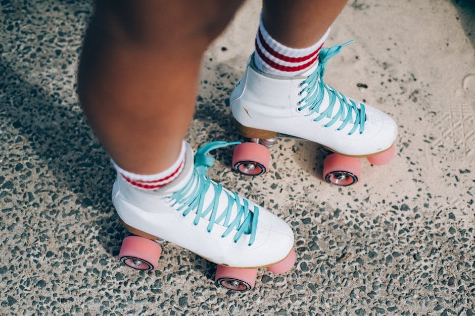 White roller skates with blue laces and pink wheels on a textured outdoor surface.