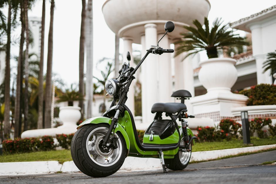 A stylish green electric moped parked in an outdoor urban setting during the day.