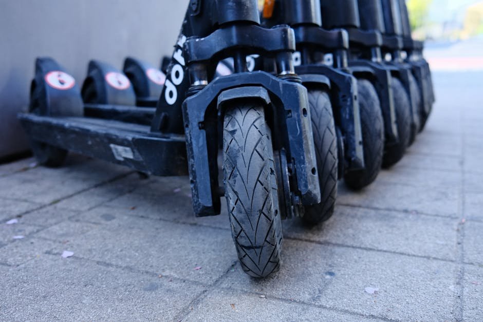 Row of parked electric scooters on a city sidewalk, focusing on wheels.